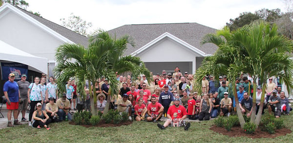 Sergeant Justin Callahan holding his youngest child posing with all the Homes For Our Troops volunteers in front of the house built for his family