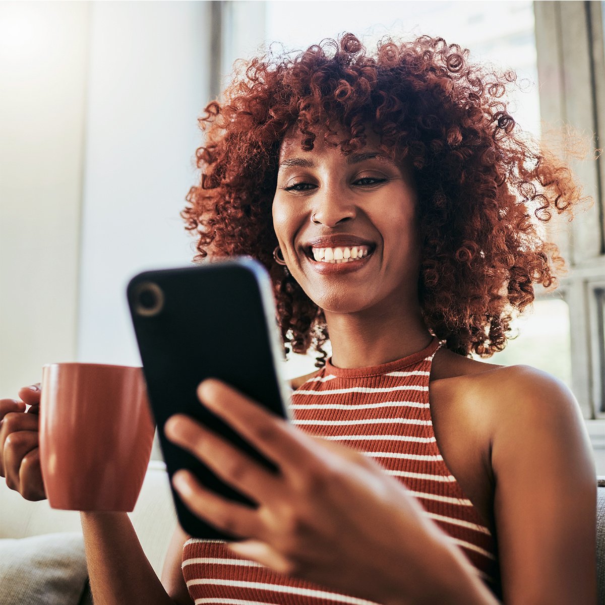 Young woman holding a mug and looking at mobile phone