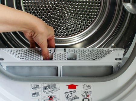 A housewife holds a lint trap from a front-loading tumble dryer.