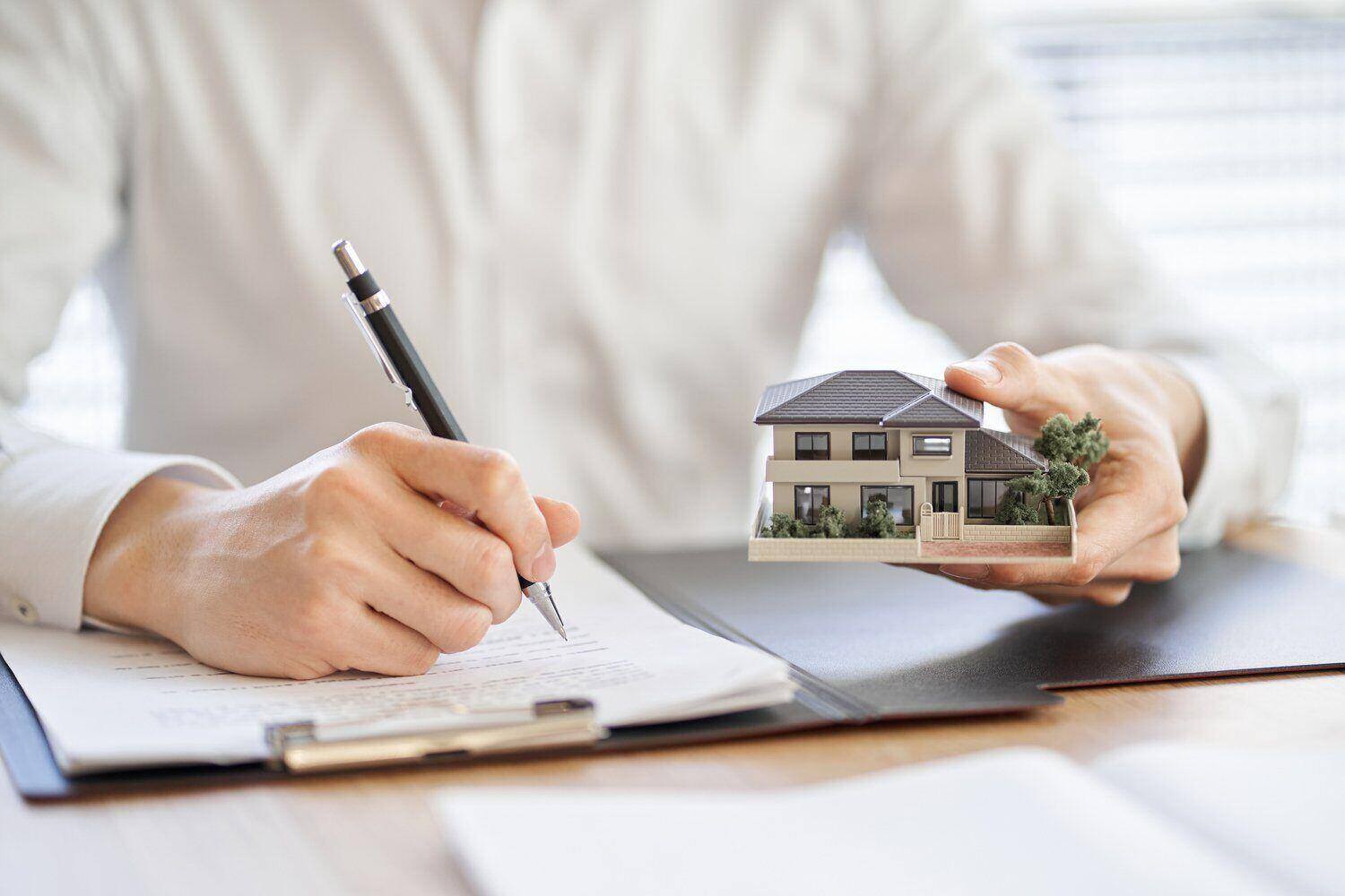 Man holding a pen and small model home while choosing the best home warranty for his house
